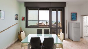 A dining area with a table and chairs, a refrigerator, and a view of the sea through large windows. - 3535 Appartamento Antares by Barbarhouse (Porto Cesareo)
