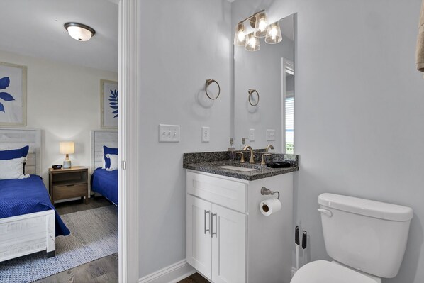 A modern bathroom with a white toilet, granite countertop, and a large mirror.