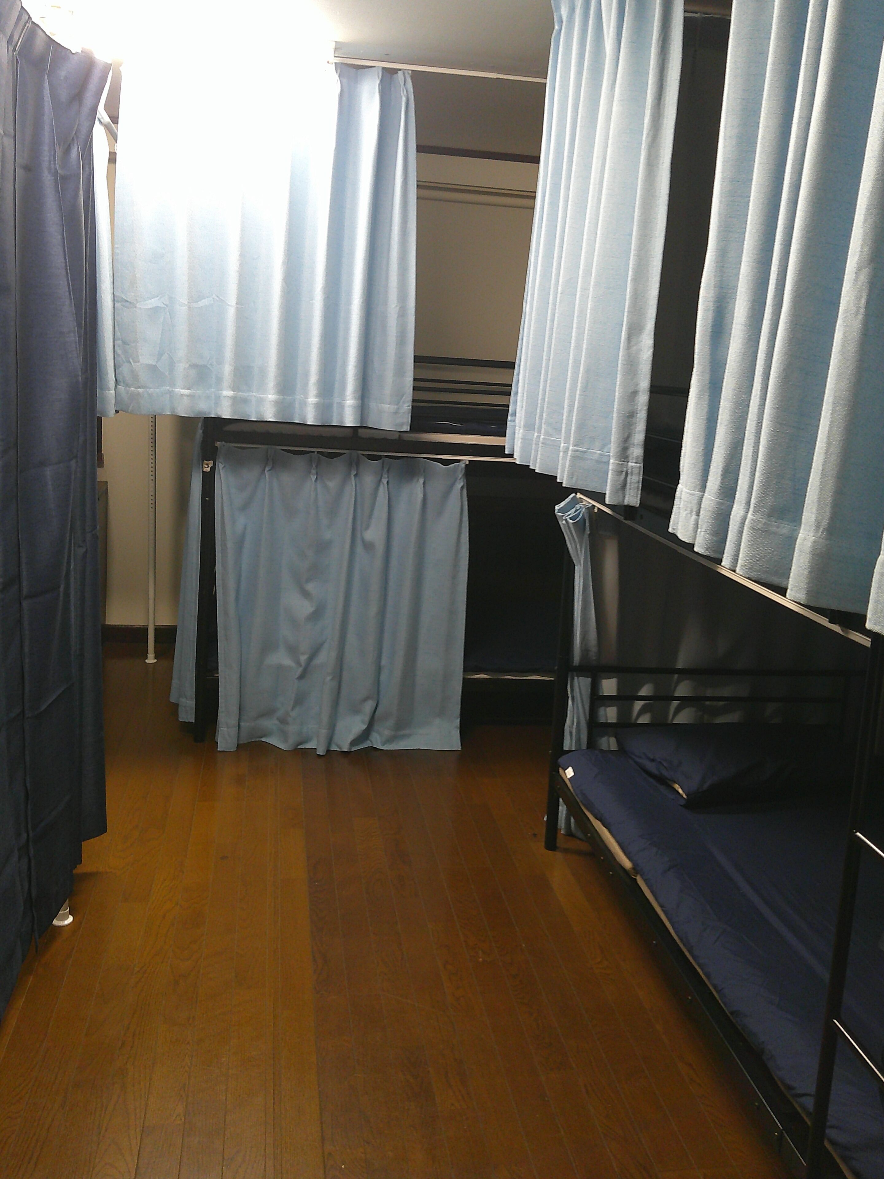 A dormitory room with bunk beds, a wooden floor, and curtains.