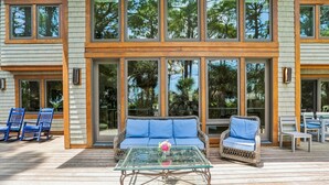 Una casa moderna con amplios ventanales y una terraza con mobiliario de mimbre y una mesa de vidrio.