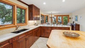 Una cocina con armarios de madera, una isla grande y vistas a árboles a través de las ventanas.