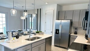 Una cocina moderna con una isla grande, electrodomésticos de acero inoxidable e iluminación colgante.