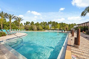 Une piscine avec des chaises longues, un mur en briques et des palmiers.