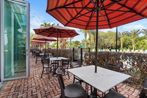 Une terrasse extérieure avec des tables et des chaises, des parasols à rayures rouges et un sol en briques.
