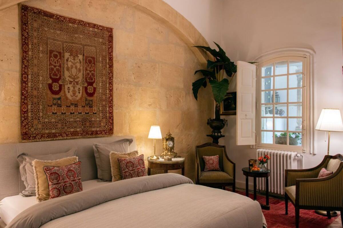 A bedroom with a large bed, a wall tapestry, a window with a view, and a radiator.