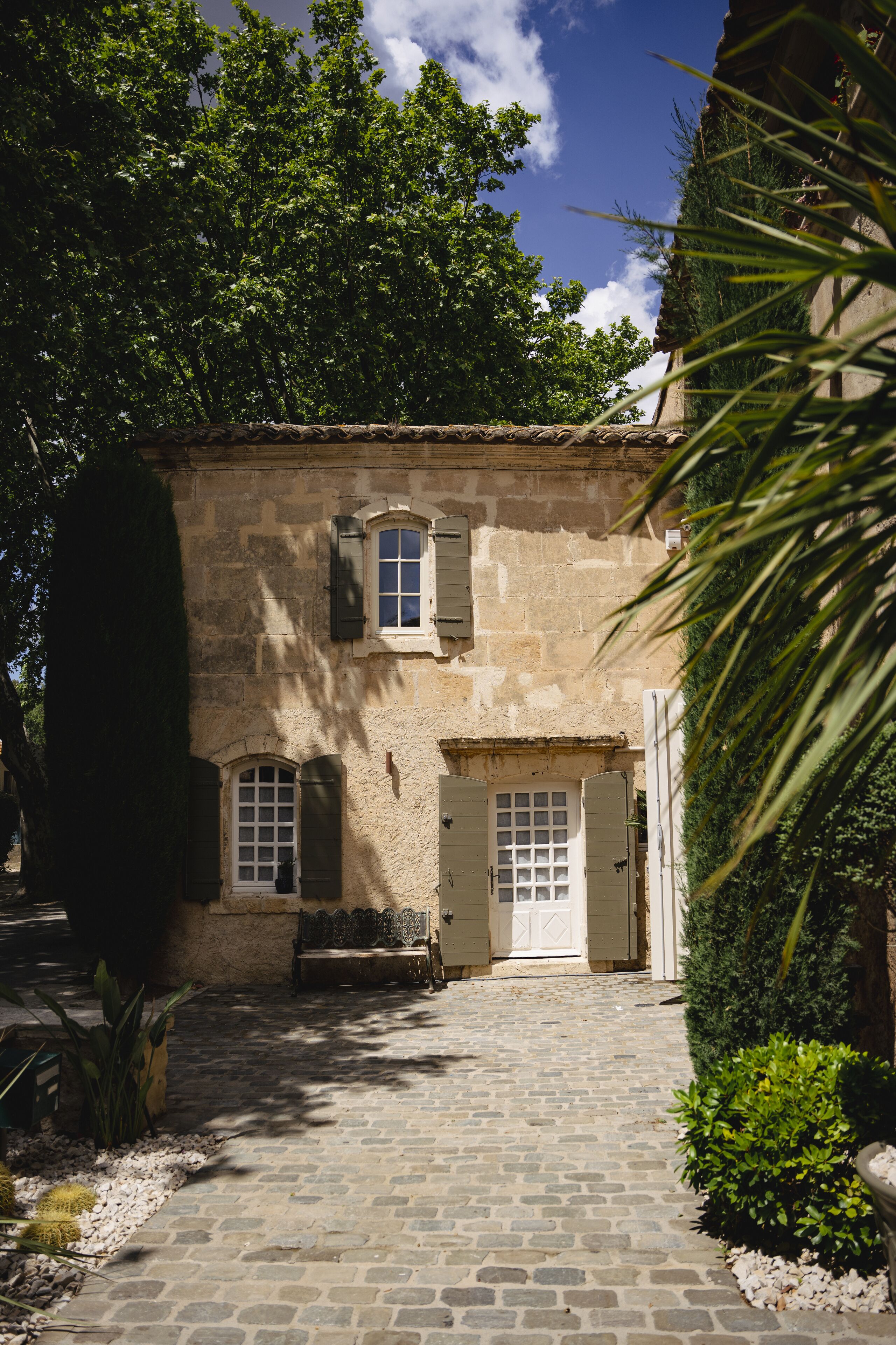 A stone building with a cobblestone courtyard, a bench, and a small garden area.