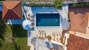 Vue aérienne d’une propriété résidentielle dotée d’une piscine, d’un espace de détente extérieur et d’un toit recouvert de tuiles.