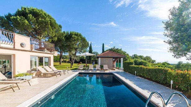 Une piscine avec des chaises longues, une pergola et un petit kiosque dans un jardin aménagé.