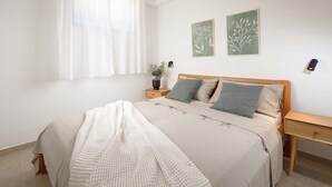 Une chambre à coucher comprenant un lit, des tables de chevet, une fenêtre avec des rideaux et deux œuvres d’art accrochées au mur.