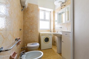 A compact bathroom with a toilet, washing machine, sink, and a window. - 3458 Approdo sul Mare by Barbarhouse (Porto Cesareo)