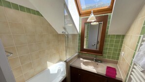 Une salle de bain avec une baignoire, un lavabo, un miroir et une fenêtre de toit.