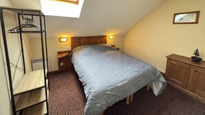 Une chambre avec un lit superposé, une lucarne, une tête de lit en bois, une table de chevet, une lampe, une commode et une petite plante.