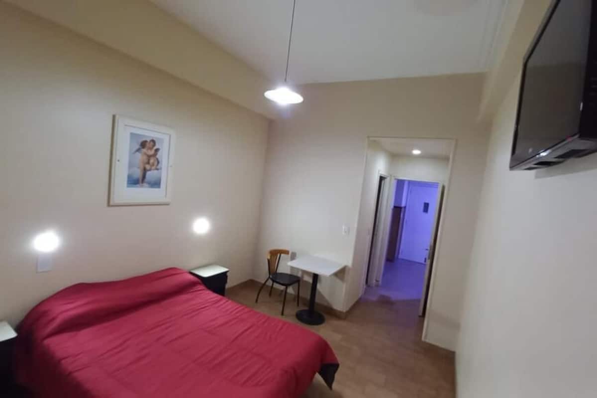 A bedroom with a bed, a desk, a chair, and a TV.