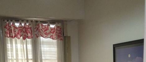 A room with two single beds, a window with sheer curtains, a wall-mounted picture, and a hanging light fixture.