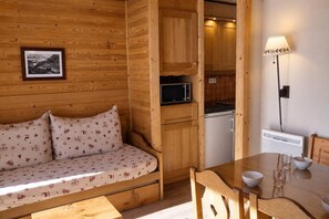 A cozy cabin interior with a wooden sofa, a dining table, and a kitchenette.