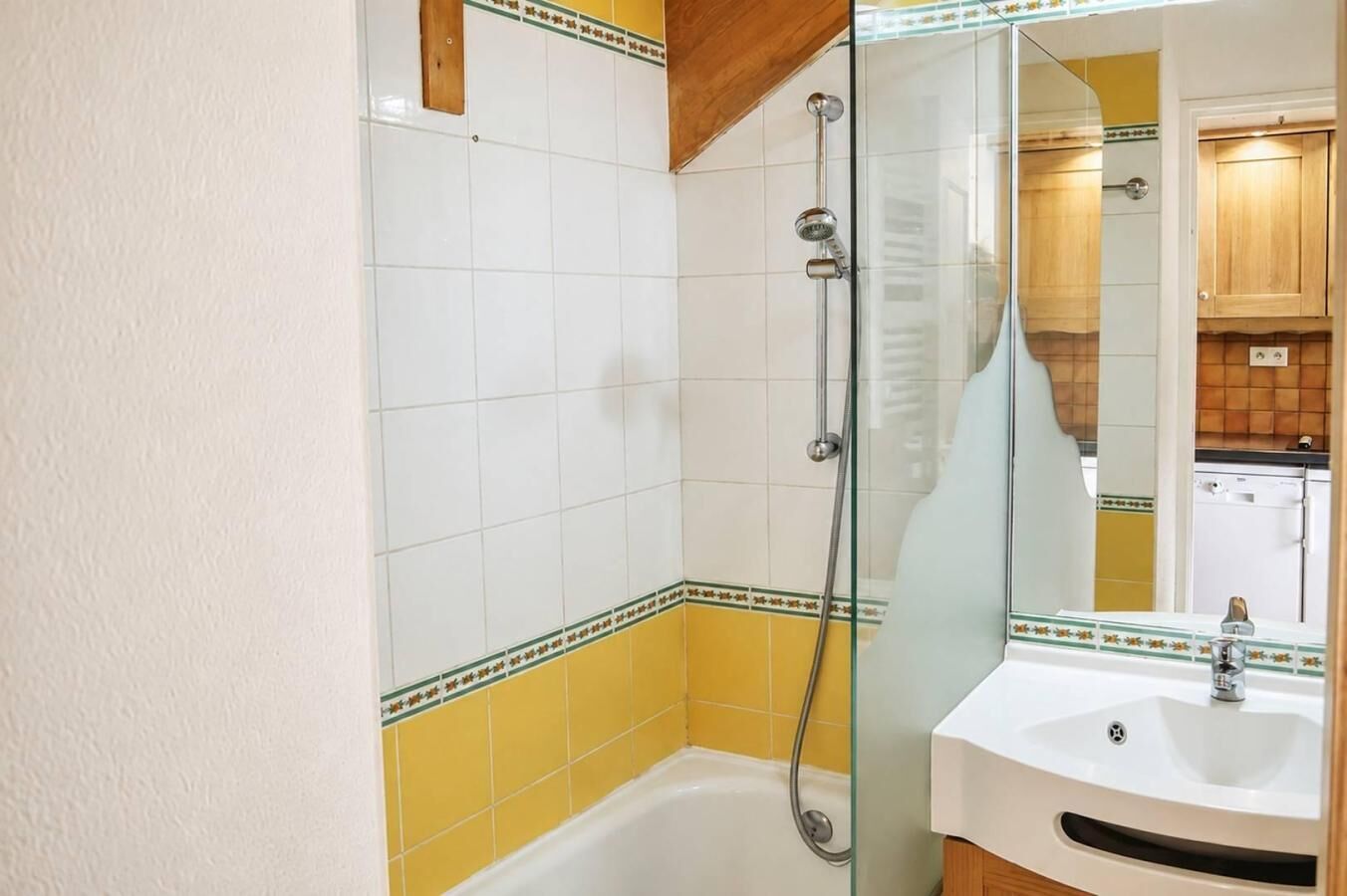 Un baño con cabina de ducha de vidrio, un lavabo blanco y pared con azulejos amarillos.