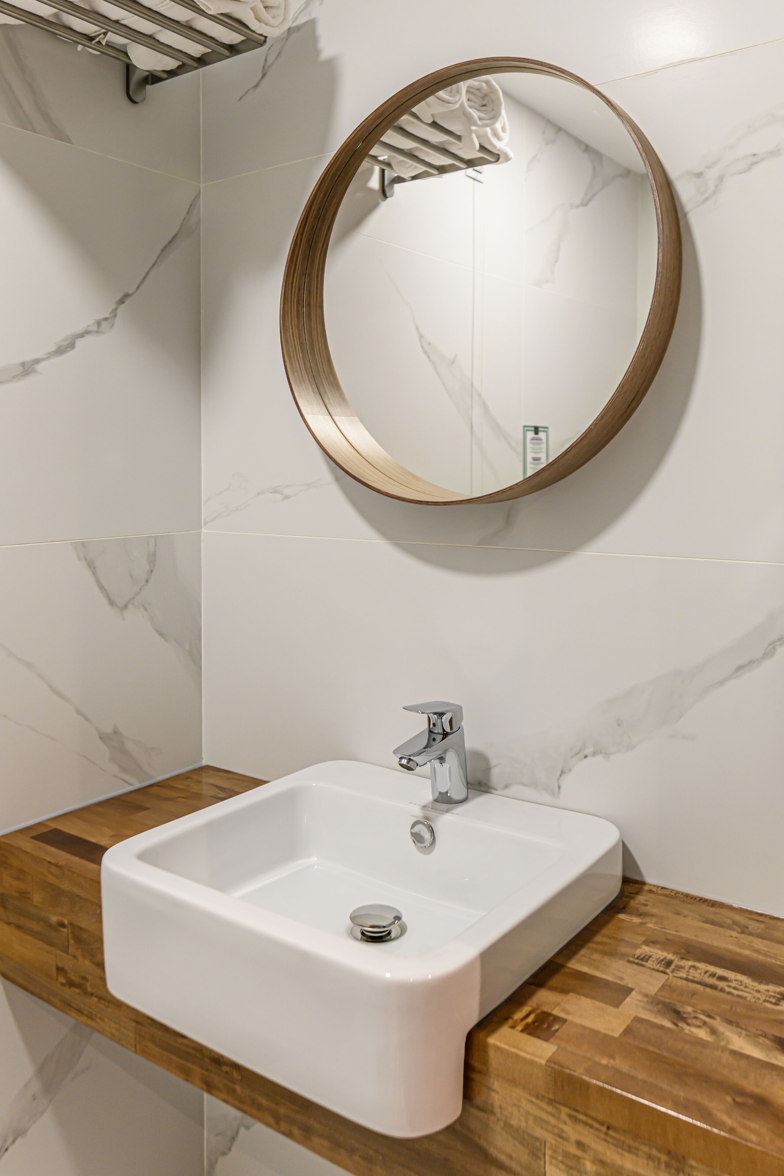 A bathroom with a white sink, wooden countertop, and a round mirror with a wooden frame.