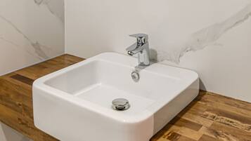 Un baño con lavamanos blanco, encimera de madera y un espejo redondo con marco de madera.
