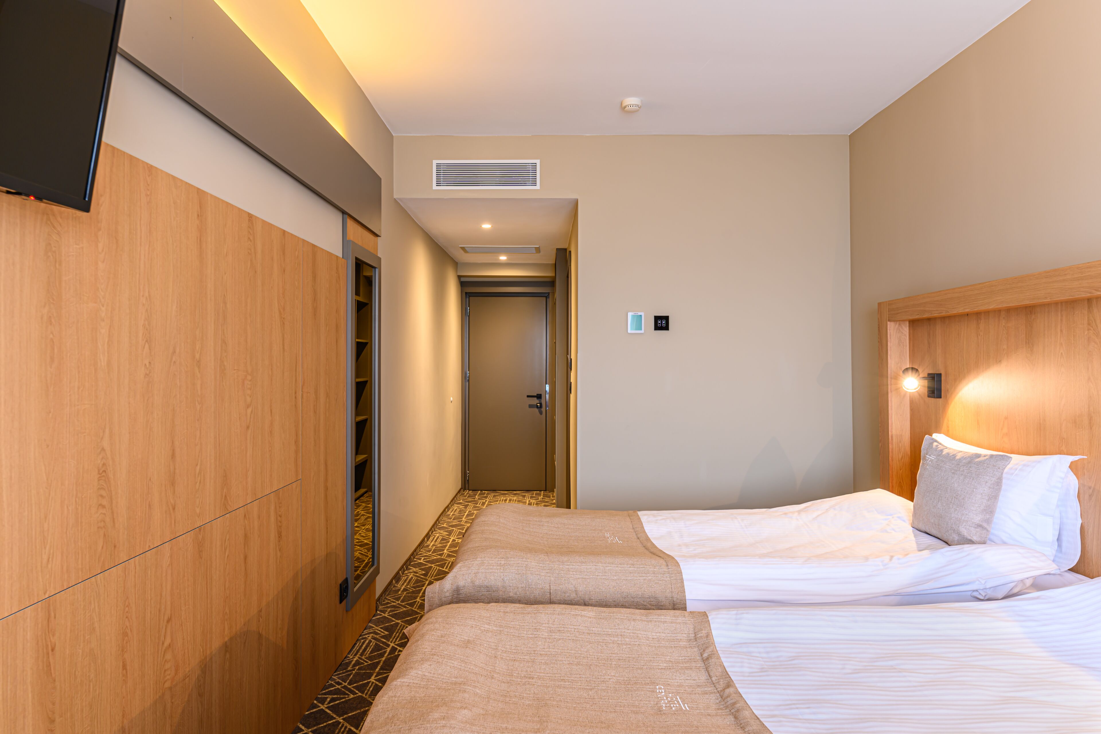 Habitació d'hotel amb dos llits, un armari, una televisió i una porta que dona a un passadís.