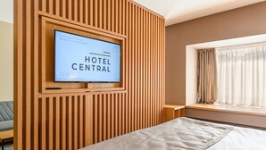 A hotel room with a bed, a TV mounted on a wooden panel wall, a window with curtains, and a small table. - Hotel Central Pascani (Pascani)