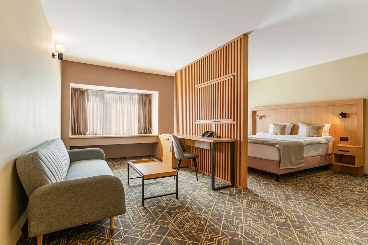 A hotel room with a bed, a desk, a chair, a sofa, and a window with curtains.