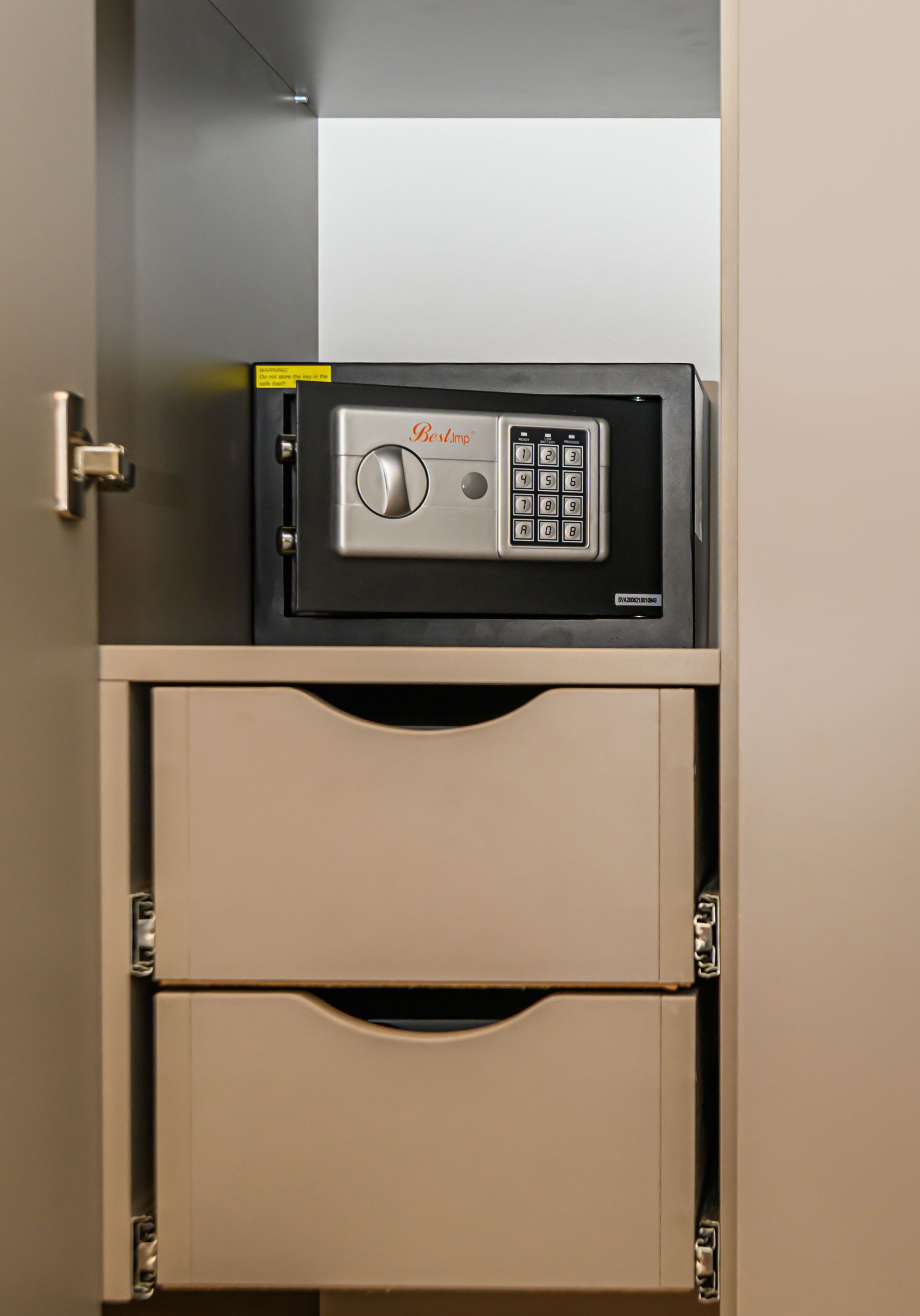 A safe deposit box with a combination lock and a keypad, located inside a beige cabinet with a door.