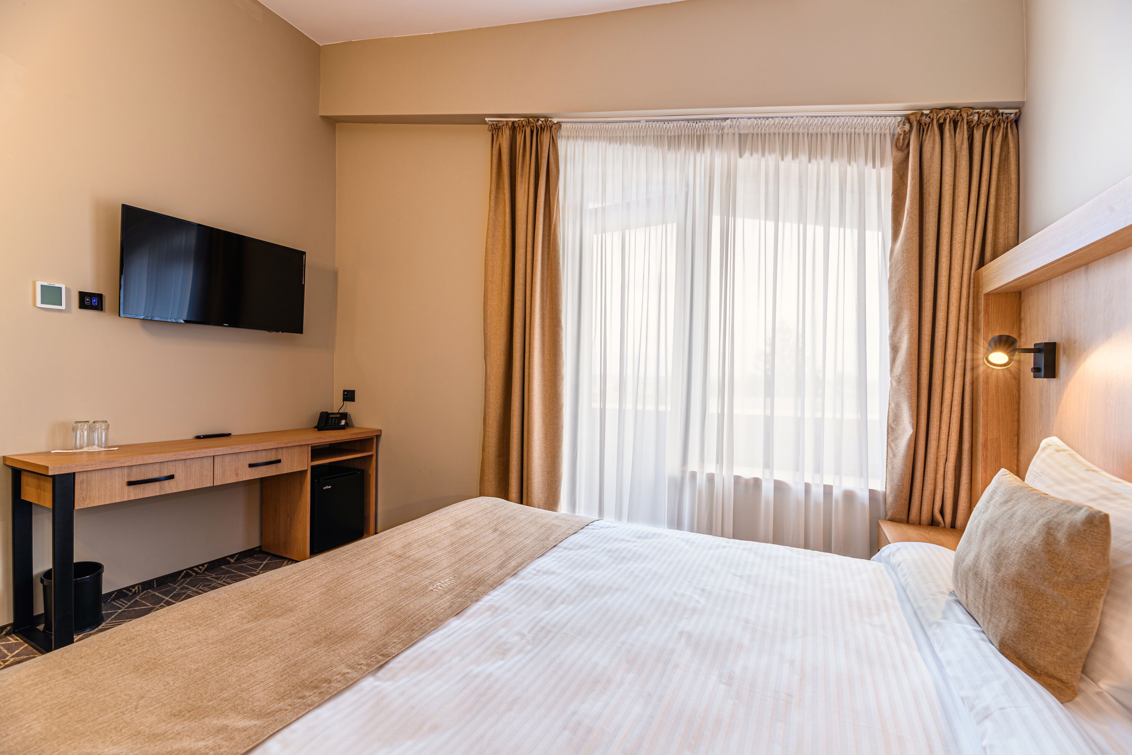 A hotel room with a bed, a desk, a television, and a window with curtains.