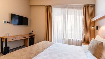 A hotel room with a bed, a desk, a television, and a window with curtains.
