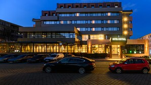 A hotel with multiple floors, a well-lit entrance, and a parking area with several cars. - Hotel Central Pascani (Pascani)