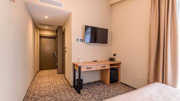 Habitación de hotel con cama, escritorio con cajones, televisor montado en la pared, refrigerador pequeño y piso con diseño.