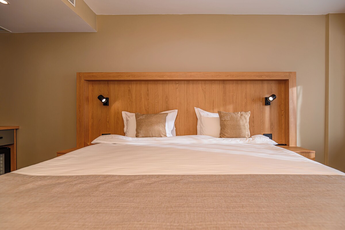 Una cama bien hecha con cabecera de madera, dos lámparas de noche y una mesita de noche con lámpara.