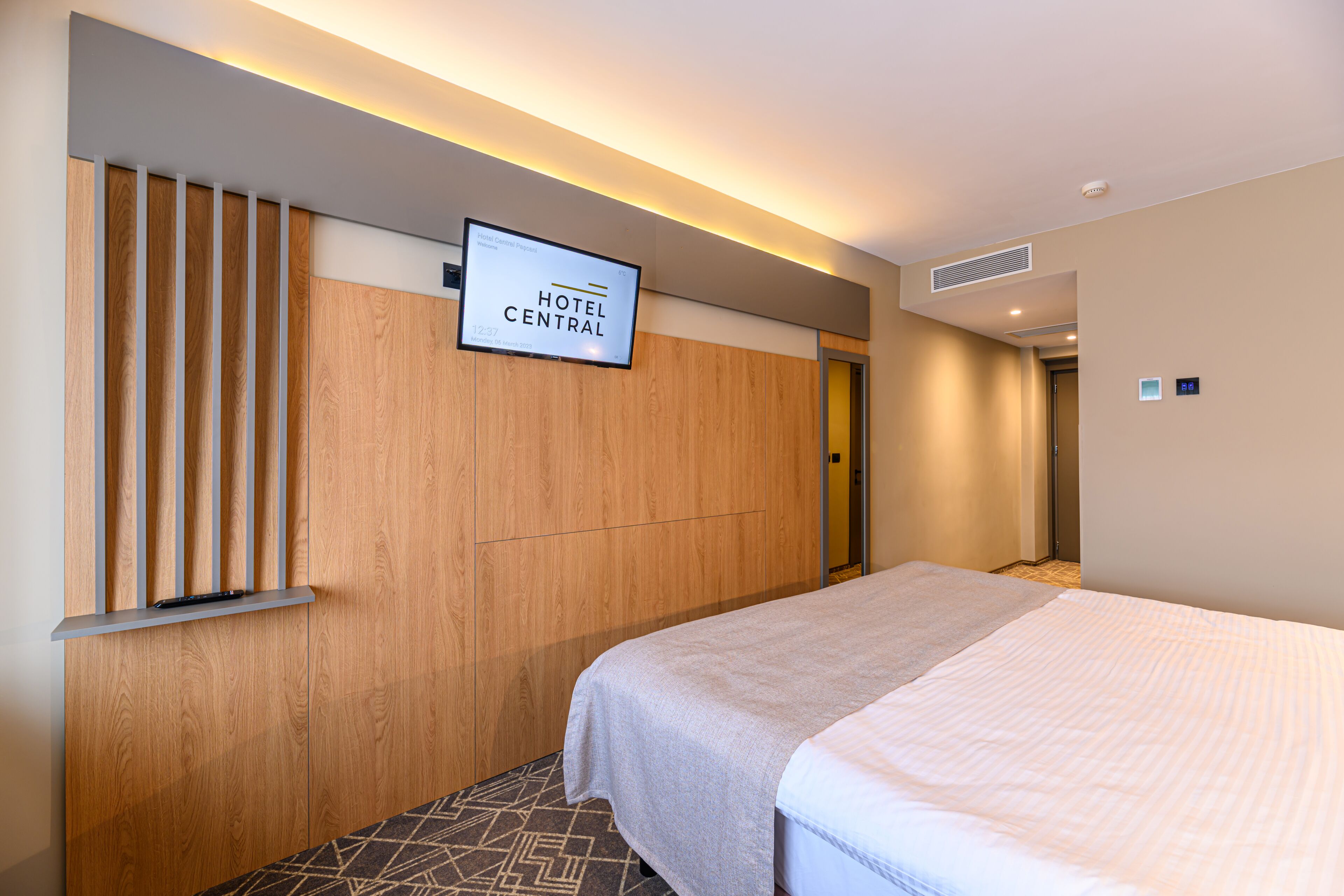 Een hotelkamer met een bed, een aan de muur bevestigde televisie en een houten paneelwand.