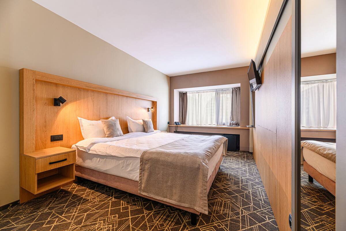 A hotel room with a bed, bedside tables, a desk, and a window with curtains.