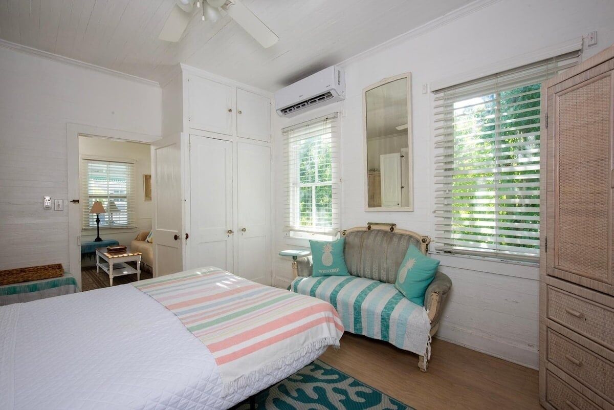A bedroom with a bed, a chair, a wardrobe, a mirror, and a window with blinds.