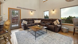 A spacious living room with a sectional sofa, a wooden coffee table, and a large window offering a view. - 3 King Beds * Game Room * Heated Garage * Trails (Lead)