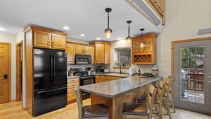 A modern kitchen with wooden cabinets, a black refrigerator, a central island with bar stools, and pendant lighting. - 3 King Beds * Game Room * Heated Garage * Trails (Lead)
