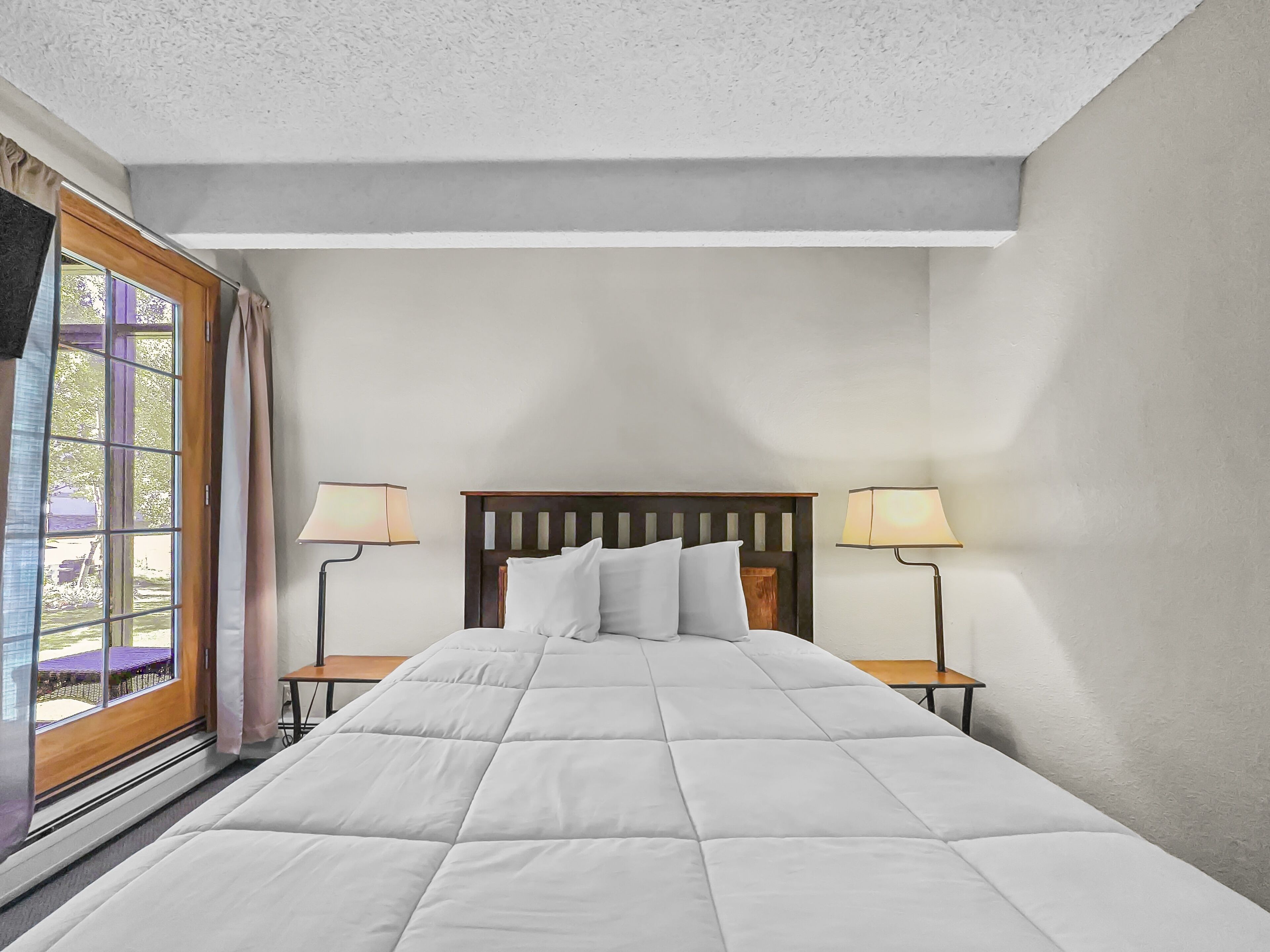 Ein Schlafzimmer mit einem großen Bett, zwei Nachttischlampen und einem Fenster mit Vorhängen.