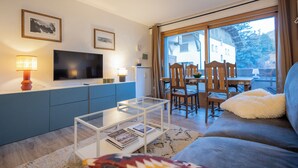 Un soggiorno moderno con televisore piatto, tavolino in vetro, divano e zona pranzo con sedie e tavolo in legno.
