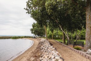 Un parque costero con un sendero de arena, árboles y bancos.