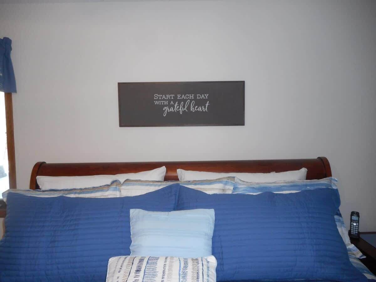 A bed with blue bedding, a wooden headboard, and a motivational quote on the wall.