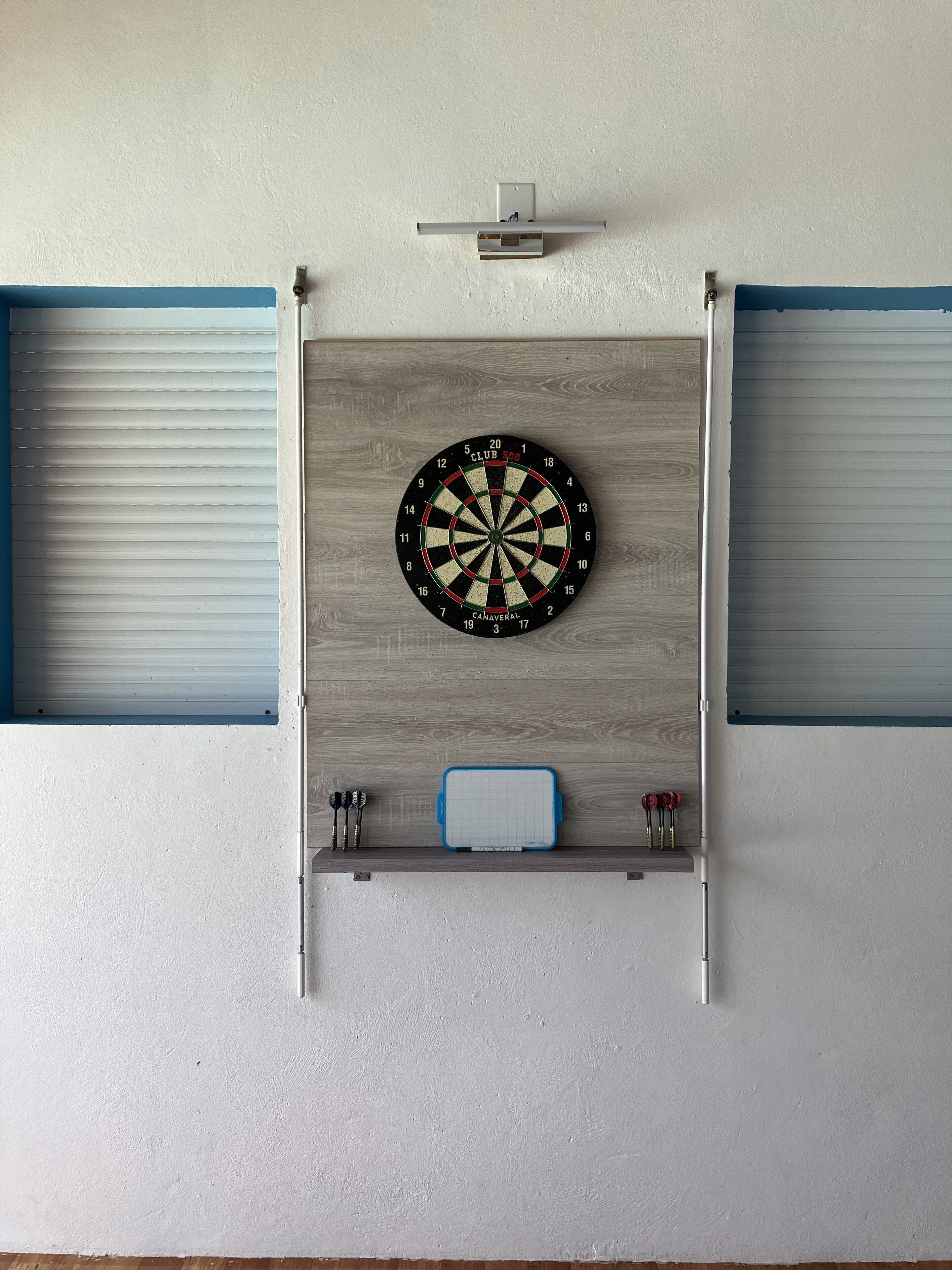 Un jeu de fléchettes fixé à un mur en bois, avec un étui pour fléchettes placé en dessous.
