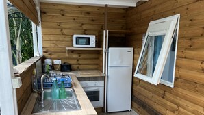 A compact kitchen with wooden walls, a microwave, a refrigerator, a sink, and a window.