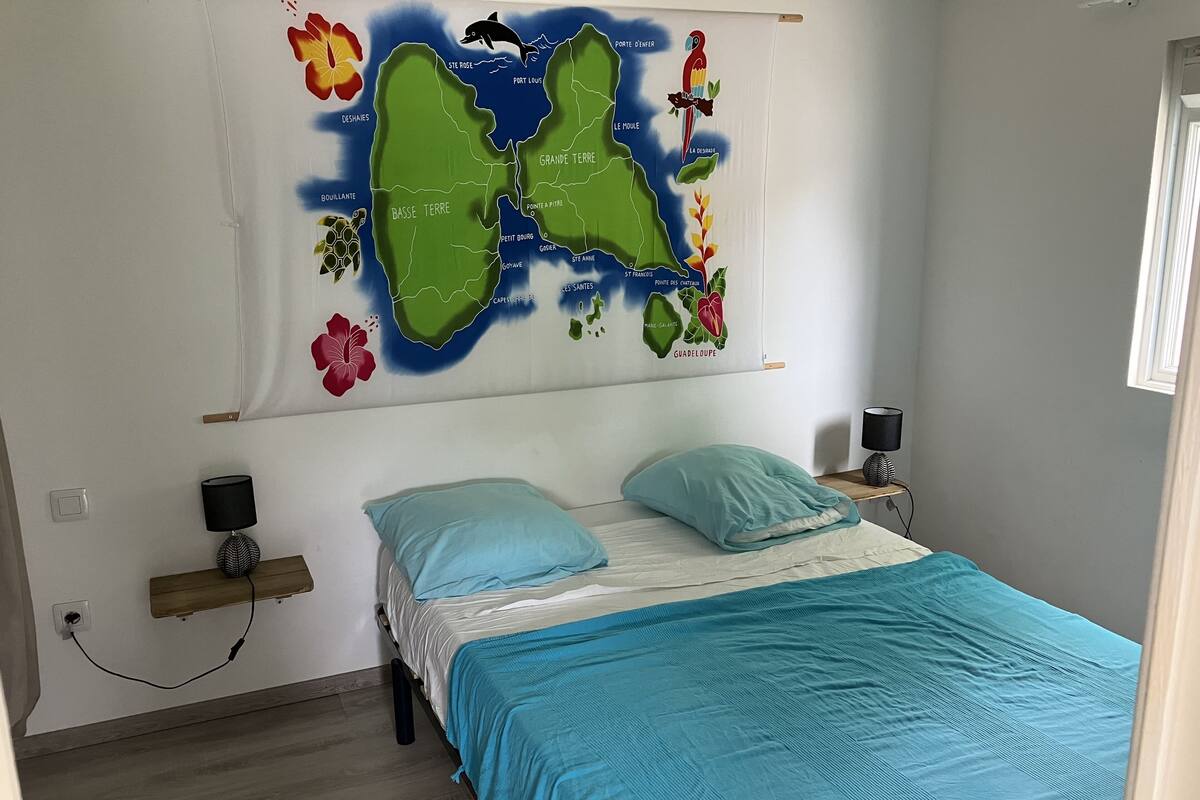 Une chambre à coucher avec un lit, deux oreillers, une table de chevet, une lampe et une carte accrochée au mur.