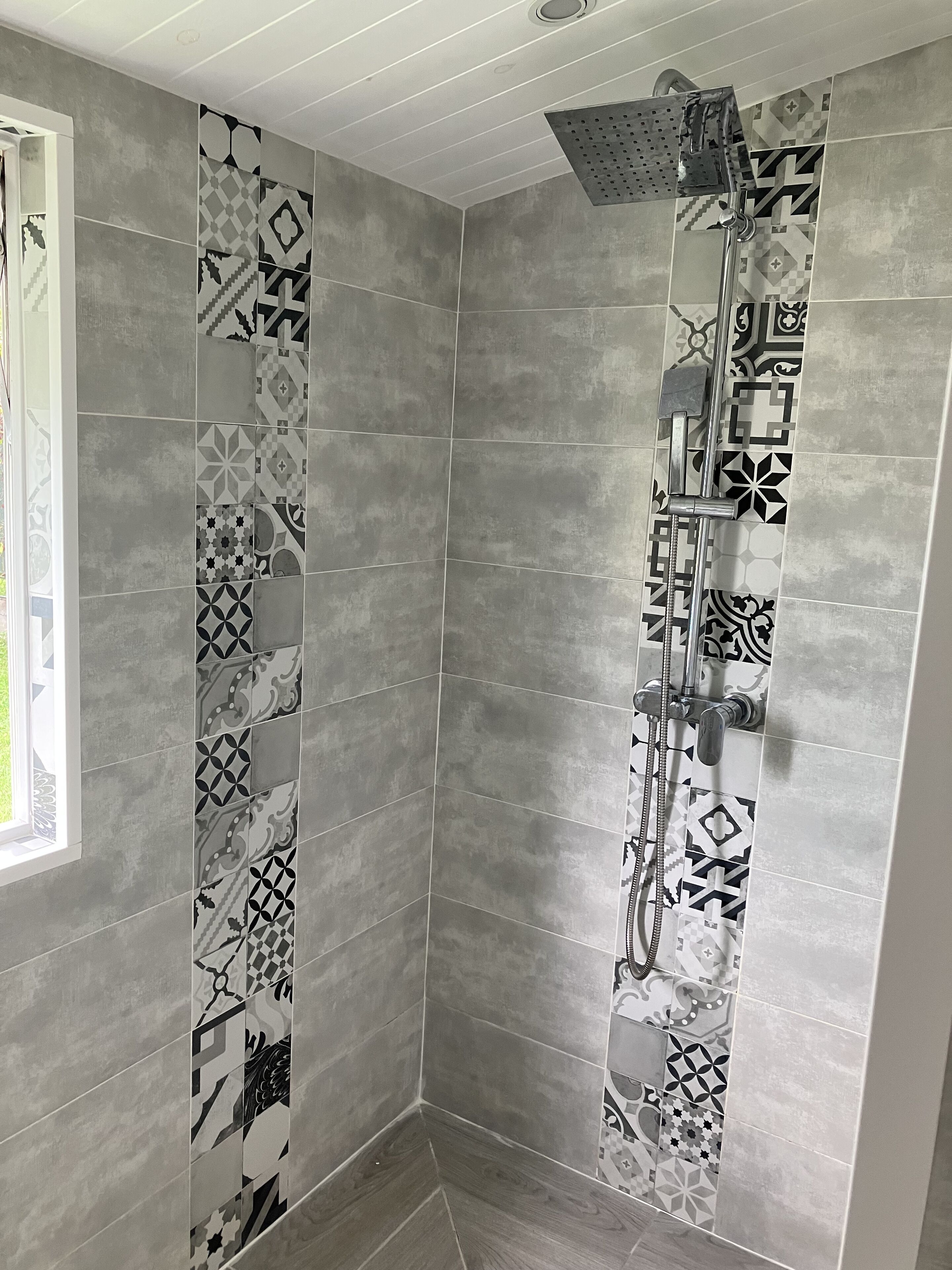 A shower area with a modern design, featuring grey tiles and a showerhead with multiple nozzles.