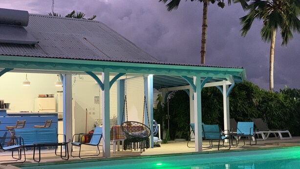 A covered pool area with lounge chairs and a dining table.
