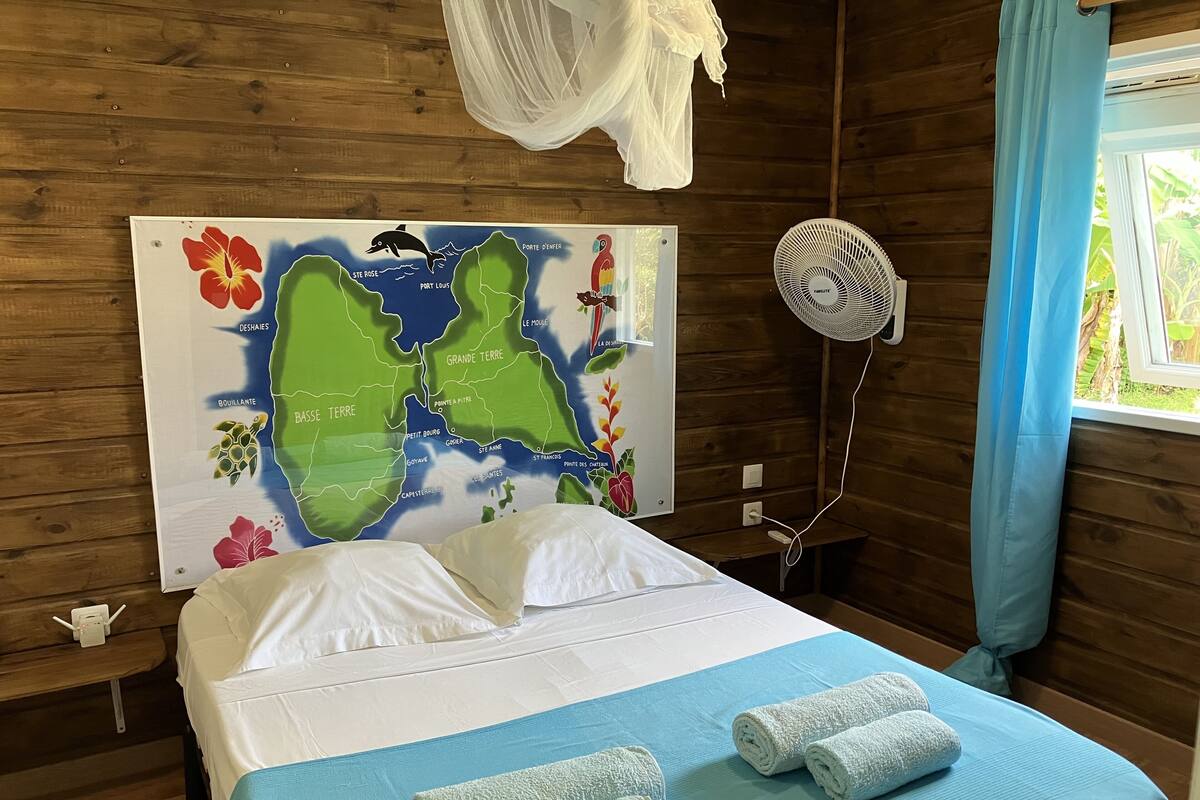 Une pièce en bois avec un lit, une carte accrochée au mur, un ventilateur et une fenêtre avec des rideaux.