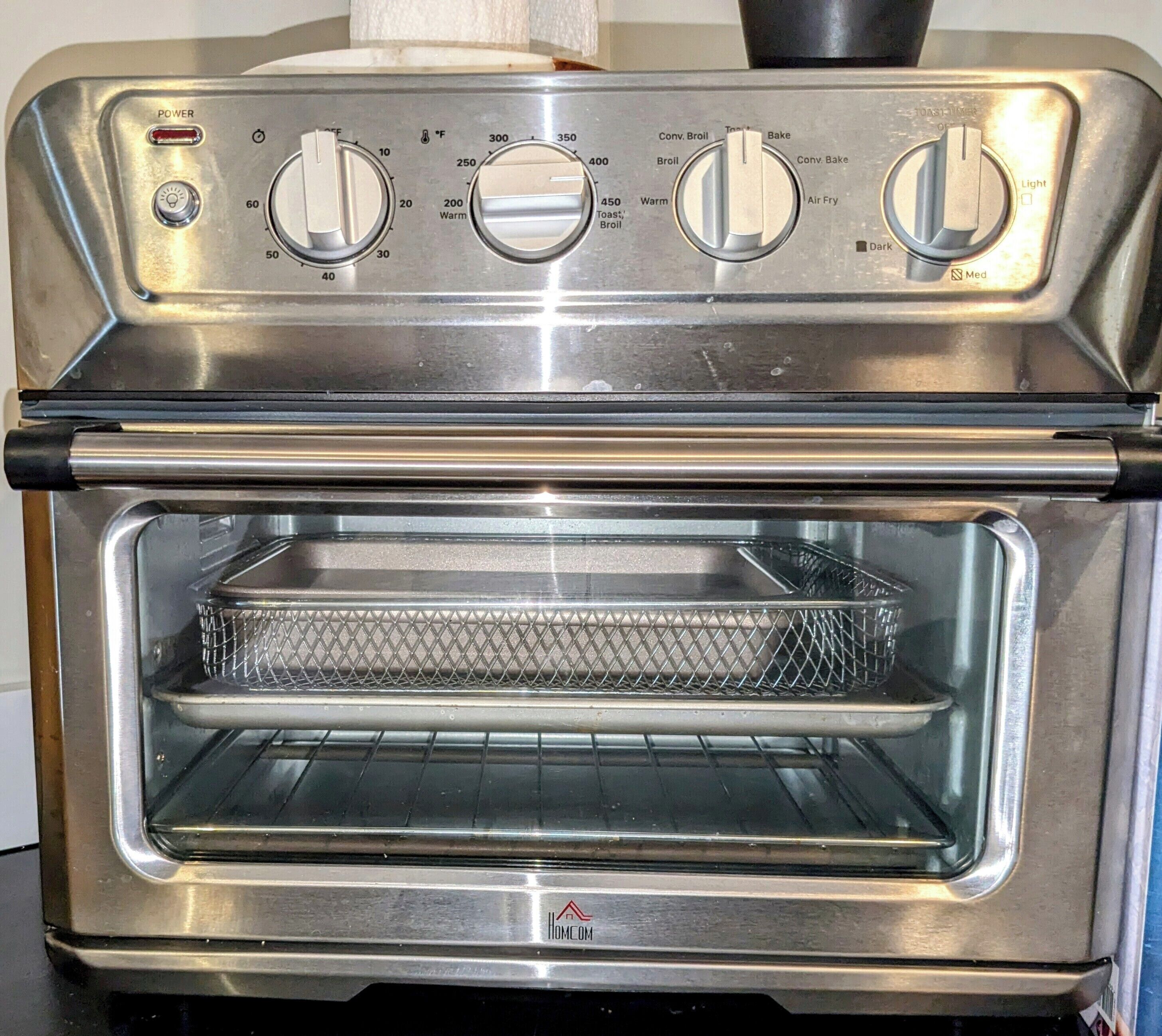 A stainless steel oven with control knobs, a wire rack, and a label reading "HomeCom."