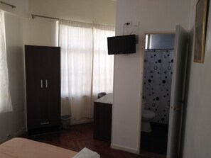 A bedroom with a bed, a wardrobe, a television mounted on the wall, and a bathroom with a toilet and shower curtain. - SUIPACHA INN HOTEL (Buenos Aires)