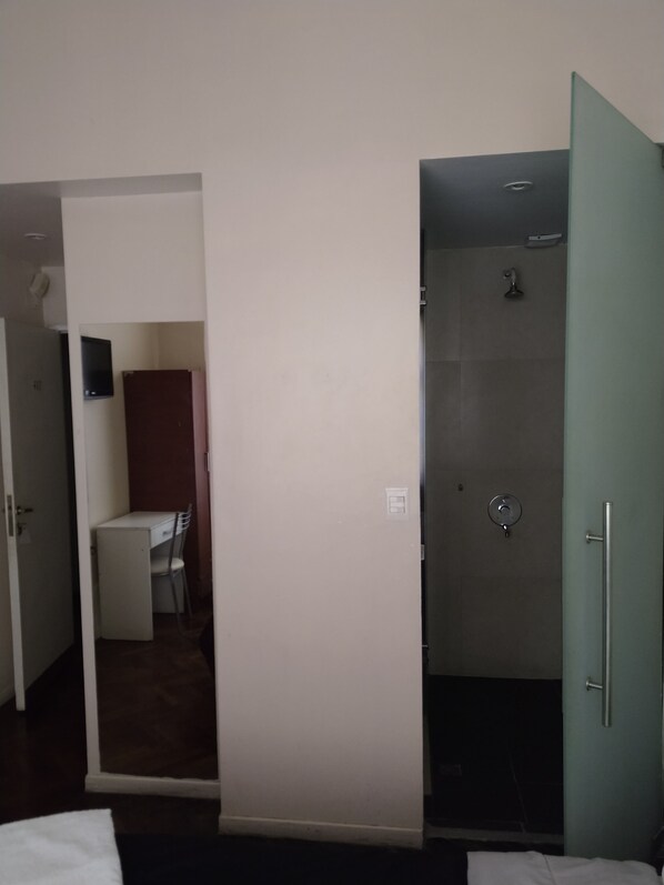 A hotel room with a bed, a shower, a desk with a chair, and a small kitchenette. - SUIPACHA INN HOTEL (Buenos Aires)