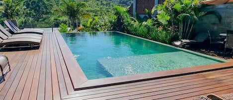 Una piscina al aire libre, sombrillas, sillones reclinables de piscina